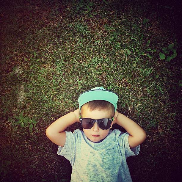 Little cool hipster Vibrant colour image of happy little baby boy lying on a green grass with his hands up on a beautiful spring day. // mobile stock photo, made with iPhone 5 rap kid stock pictures, royalty-free photos & images