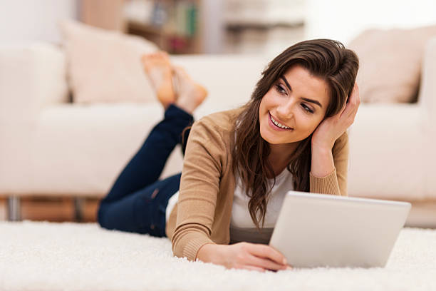 istock Beautiful woman holding her tablet while lying down on carpet 481992081