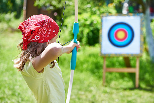 Girl with bow shooting to sport aim in sunny summer day
