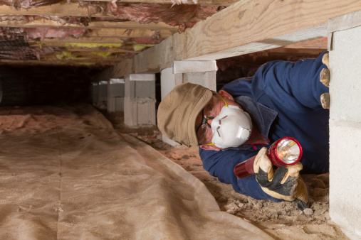 Termite inspector in residential crawl space inspects a pier for termites.