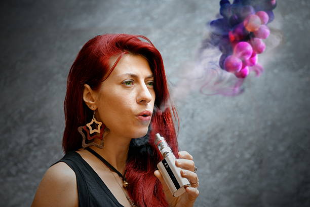 elegante donna fumare una sigaretta elettronica esterna ufficio edificio - smoking women smoke smoking issues foto e immagini stock