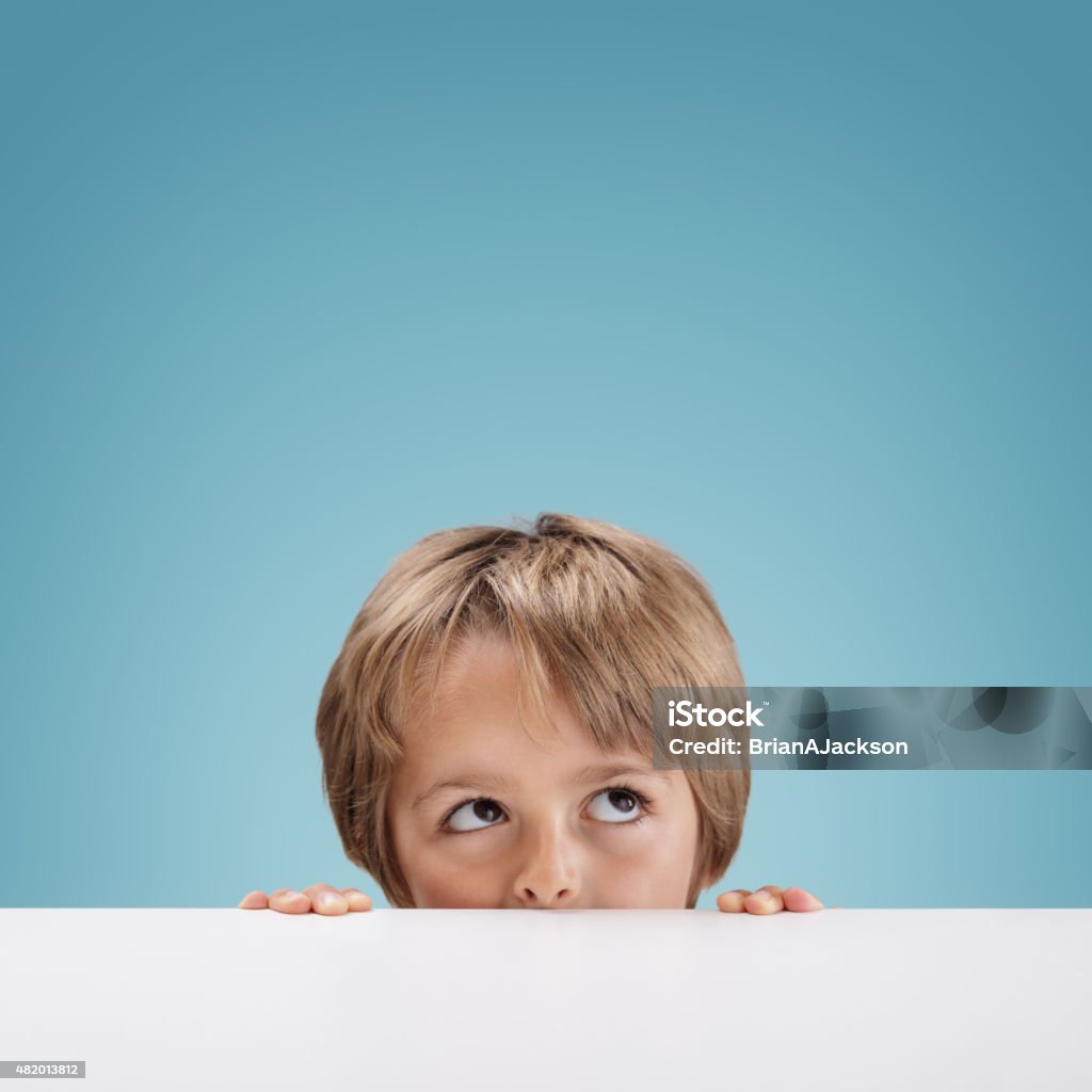 Boy peeking over a white board Young boy peeking over a white board looking up at copy space for a message Child Stock Photo