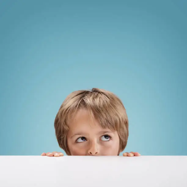 Young boy peeking over a white board looking up at copy space for a message