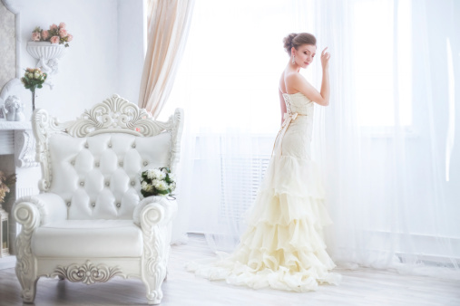 the bride sits on a antique chair with a bouquet in a wedding dress indoor