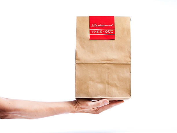 Hand Delivering Takeout Delivery Fast Food Bag Package Container A takeout deliveryman delivering convenience fast food package paper bag container to customers. Isolated and cut out on white background. Hand holding a brown bag of take out food with a red restaurant label. Photographed close-up in studio. fast food restaurant stock pictures, royalty-free photos & images