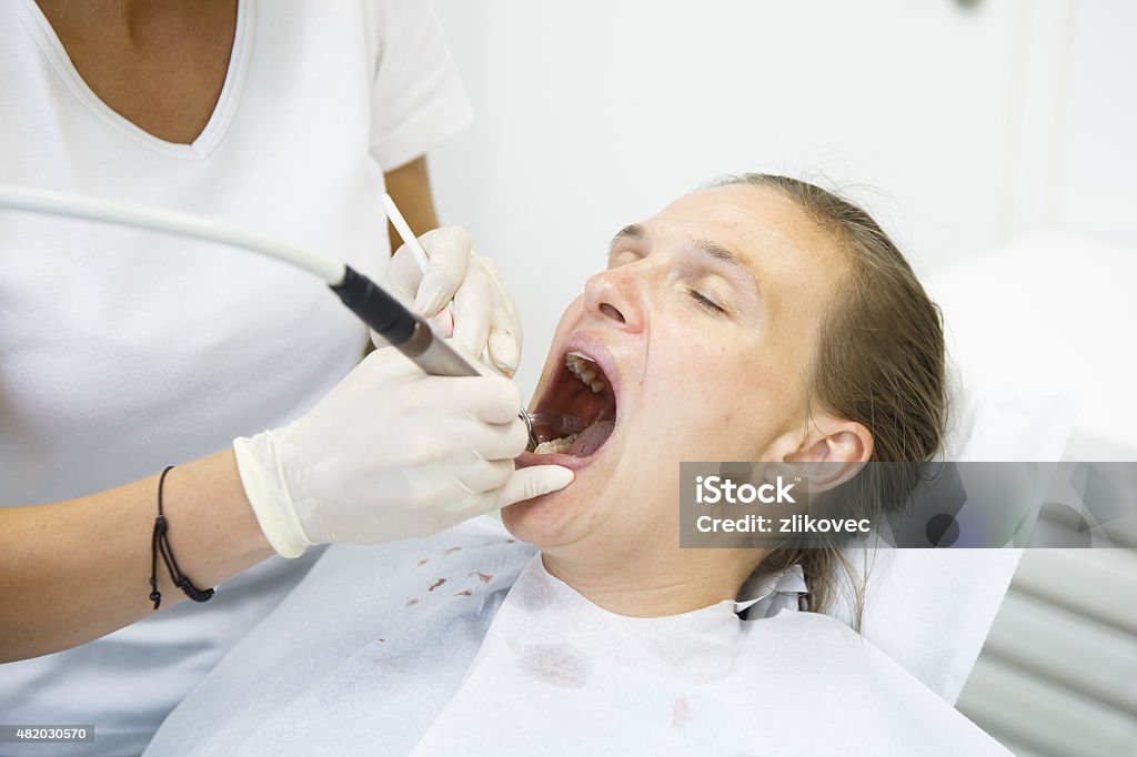 Woman at dentists office Woman at dentists office, getting her teeth examined and cleaned of tartar and plaque, preventing periodontal disease. Dental hygiene, painful procedures and prevention concept. Dental Equipment Stock Photo