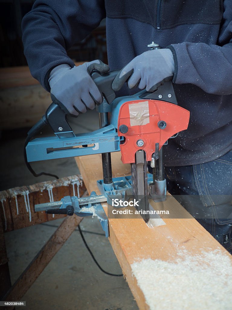 man with chain mortiser mill-cuts a wooden board Close-up of the hands of a man with chain mortiser cutting a wooden board 2015 Stock Photo