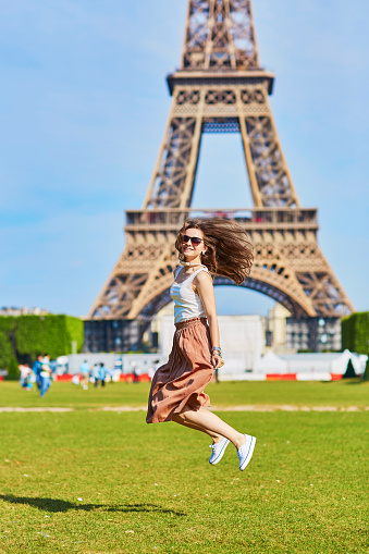 Beautiful young woman in Paris jumping near the Eiffel tower on a summer day