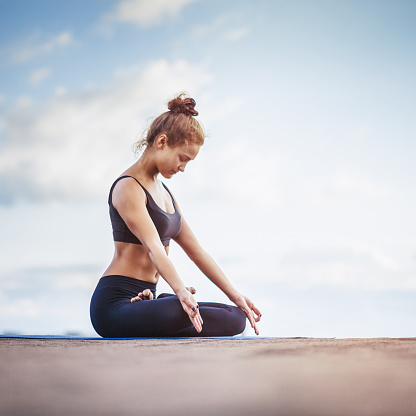 Young pretty woman meditating outdoors on a rooftop. High Key Toned. Stock photo.