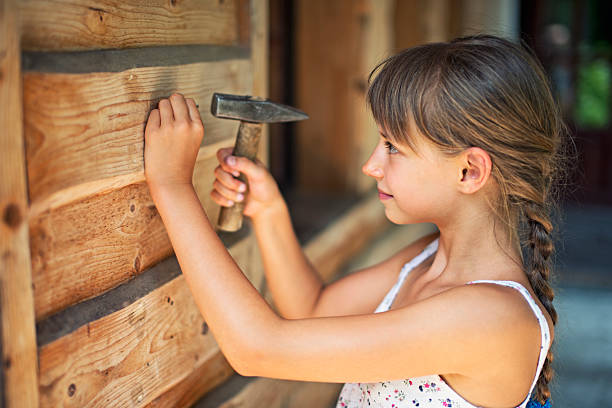 Little girl hammering a nail Little girl aged 9 hammering a nail to the wooden cabin wall. The smiling girl is practicing the ability to correctly hammer a nail. girl with a hammer stock pictures, royalty-free photos & images