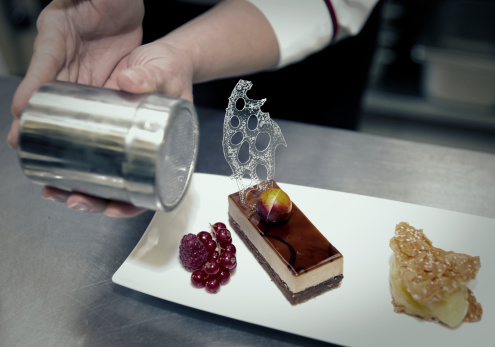 Professional pastry chef is decorating a dessert with sugar powder