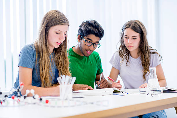 Chemistry Lab Experiments A multi-ethnic group of college age students are sitting together in a chemistry class, working on an assignment, taking notes on the amount of solvent in their beaker. high school high school student science multi ethnic group stock pictures, royalty-free photos & images