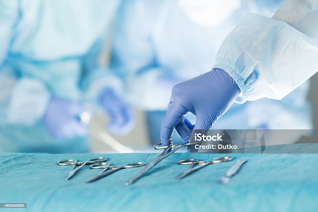 Close-up of scrub nurse taking medical instruments Close-up of scrub nurse taking medical instruments for operation with colleagues performing in background Surgery Stock Photo