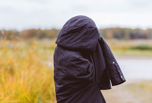 man in a black jacket with a hood covering her face