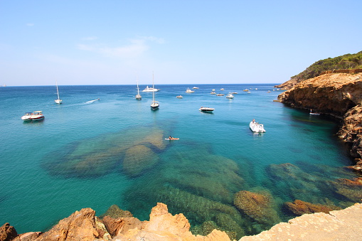 Several boats sail through crystal waters close to beautiful village and beach of Sa Riera, Mediterranean sea, Catalonia, Spain
