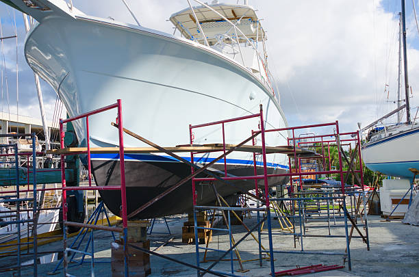 Boatyard repair big powerboat on racks surrounded with work scaffolding Very large fishing sportboat is getting repair work done and is on racks surrounded with work scaffolding at a busy boatyard marina with a sailboat on work racks in the background. motorboat maintenance stock pictures, royalty-free photos & images