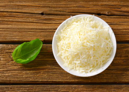 bowl of grated parmesan cheese and basil leaf isolated on wood