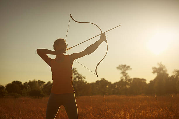 weibliche archer im feld bei sonnenuntergang - archery bow arrow women stock-fotos und bilder