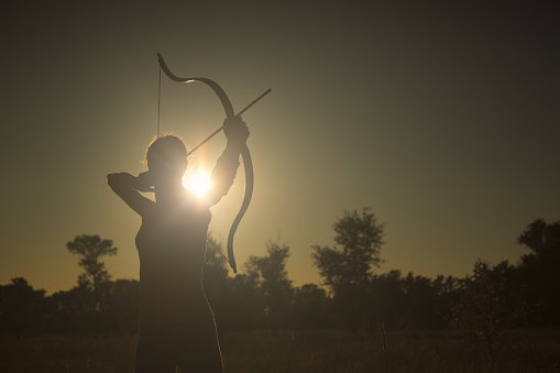 Female archer in the field at sunset
