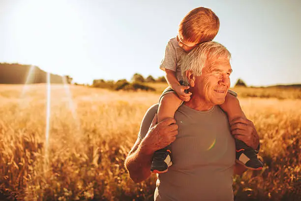 Photo of  a little boy and his grandfather, enjoying in the amazing nature. Grandfather is carrying him on his shoulders.