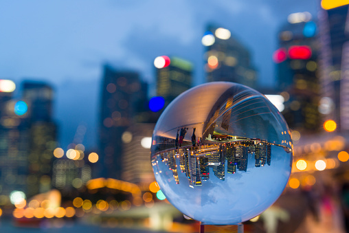 Reflection of Jubilee Bridge and Central Business District of Singapore during dusk hour in a glass ball, tourists enjoy the night scene at Jubilee Bridge.