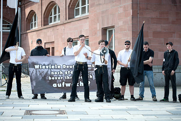Young german Neonazis Wiesbaden, Germany - May 28, 2011: A speaker of the JN (Junge Nationaldemokraten) gives a xenophobic speech demanding the forced deportation of foreign people in the city of Wiesbaden. Junge Nationaldemokraten is the youth organisation of NPD (Nationaldemokratische Partei Deutschlands). Founded in 1964 the NPD is a German nationalist party, its agitation is racist, antisemitic, revisionist. Because of its activities against the constitutional order the party is under observation of the Verfassungsschutz (German Federal Intelligence agency) national democratic party of germany stock pictures, royalty-free photos & images