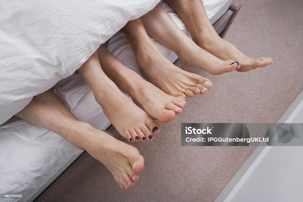 Low section of woman with two men in bed Three People Stock Photo