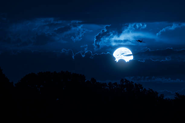 This big, bright moon illuminates the clouds and the night time sky as well as a commercial jet airliner on approach.
