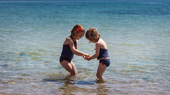 Beautiful little girls (sisters) play in the sea.
