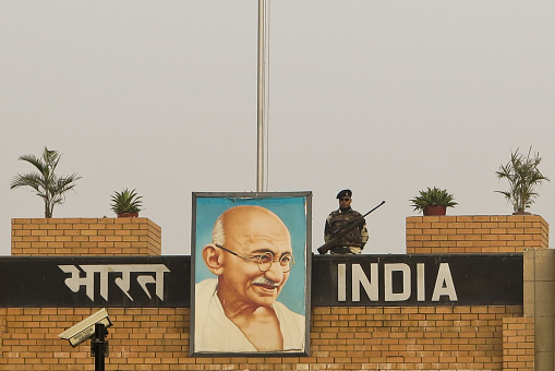 Amritsar, India - December 7, 2014: A soldier of the Indian Army on The Indian/Pakistan Border, 32km from Amritsar, India, stands guard with a painting of Gandhi at his side