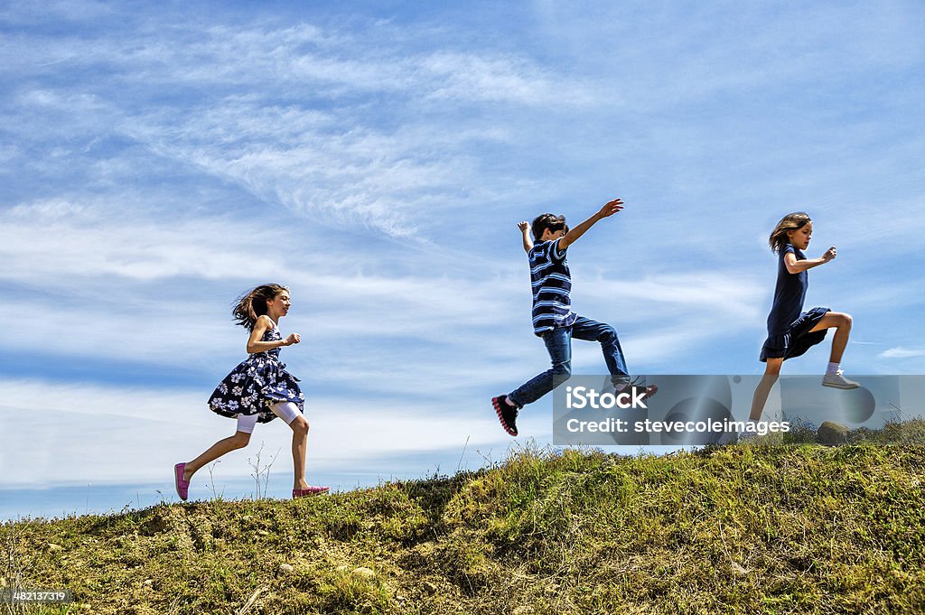 Children Playing Children skipping and jumping up a hill. Child Stock Photo