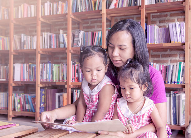 istock Mother and little daughter reading book together in library 482157088