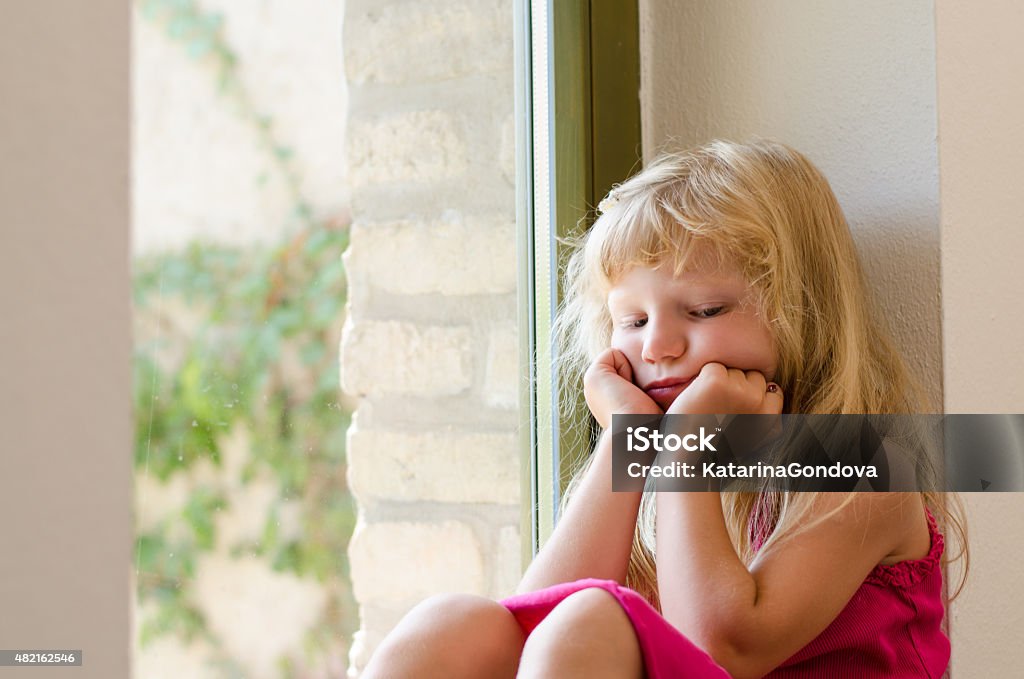 bored girl with long blond hair sitting by the window adorable bored girl with long blond hair sitting by the window 2015 Stock Photo