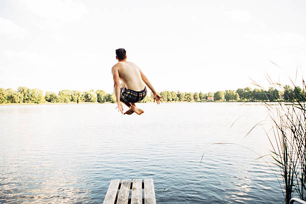 carefree summer day at lake: rear view of jumping young man as canonball into water