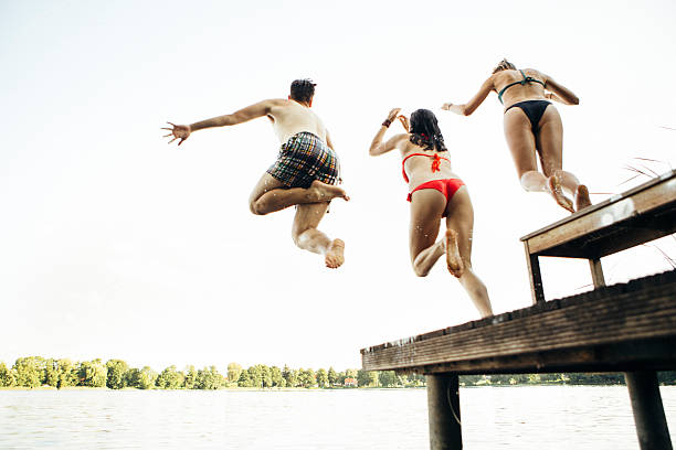 istock summer day: three young adults jump from jetty into lake 482166990