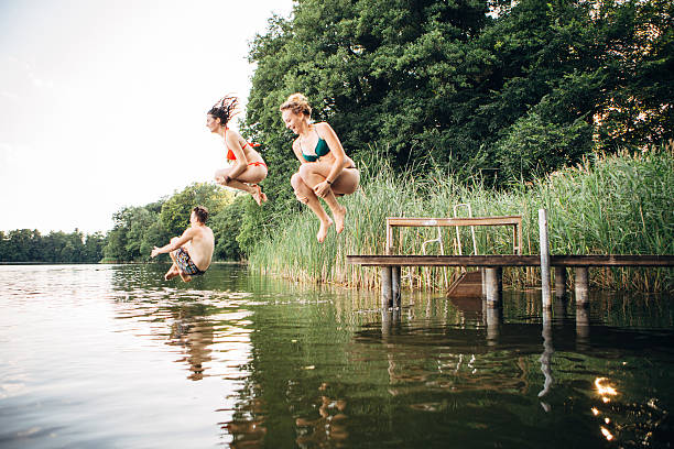 summer day: three young adults jump from jetty into lake carefree summer day: three young adults jump into lake jumping teenager fun group of people stock pictures, royalty-free photos & images