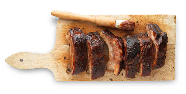 Prepped Pork Ribs on Cutting Board Thick cut BBQ pork ribs on a cutting board with sauce brush smoked pork stock pictures, royalty-free photos & images