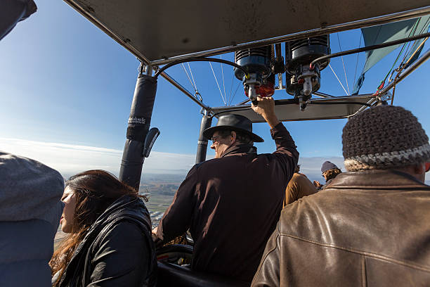 Napa, California, USA - November 28, 2014: Captain driving hot air balloon in the air. Captain driving the hot air balloon in the air and look at left side. A few tourists around him and enjoy this trip.