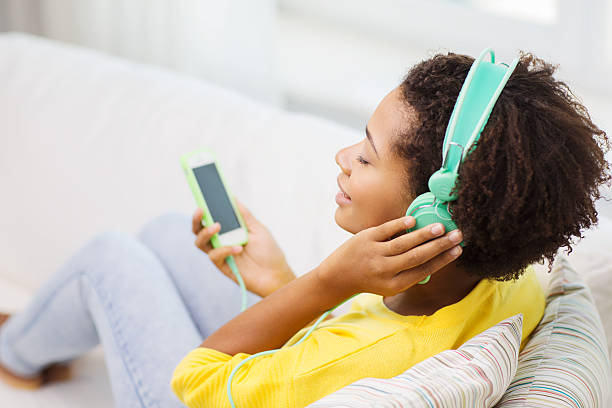 happy african mujer con smartphone y auriculares integrados - women sofa teenage girls hairstyle fotografías e imágenes de stock