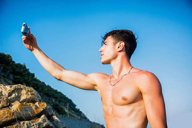 torse nu jeune homme prenant selfie photo sur la plage - shorts rear view summer beach photos et images de collection