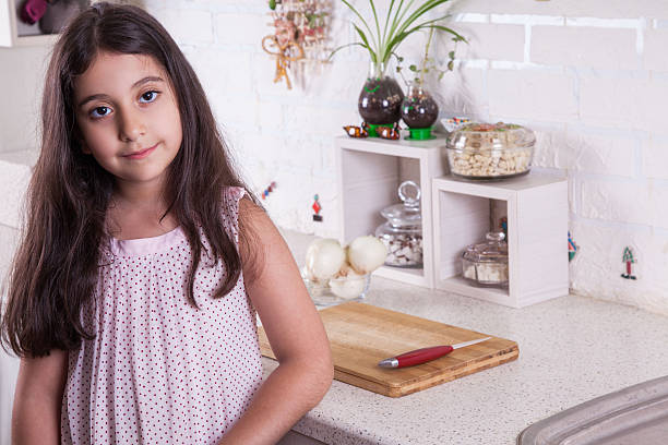 Beautiful happy girl works in the kitchen Beautiful little middle eastern 7 years old girl is working with knife and onion in the white kitchen. studio shot. looking at camera. 9 stock pictures, royalty-free photos & images
