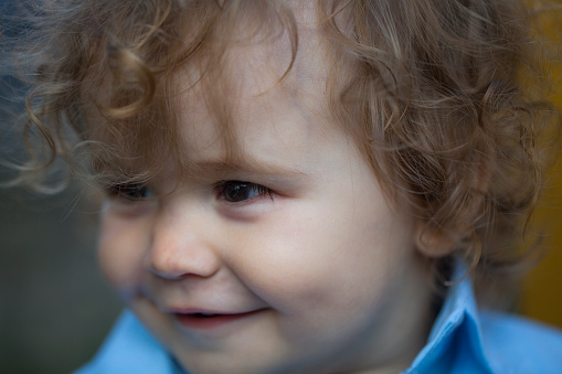 Close up portrait of a smiling happy curly white little one year old baby boy with the dimples on cheeks looking away outdoor, horizontal photo