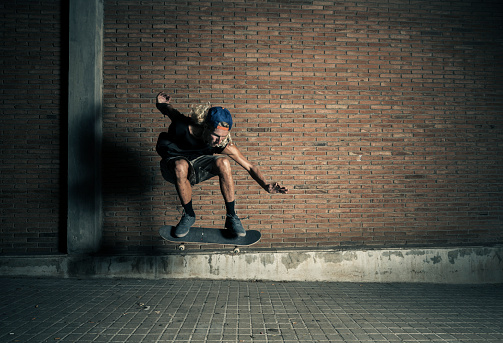 Young man jumping with skateboard against brick wall at night