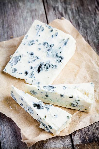 Blue cheese slices Blue cheese slices closeup on paper on rustic wooden table blue cheese stock pictures, royalty-free photos & images