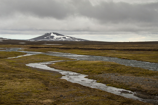 Shield volcano on Iceland in a barren landscape with small river/