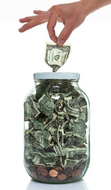 mão colocar o dinheiro em um pote cheio de dinheiro - photography still life vertical bill - fotografias e filmes do acervo