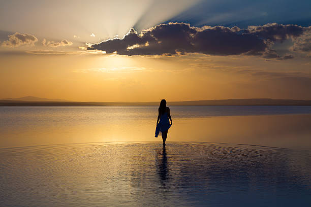 Walking into sunset Young woman walYoung woman walking at sunset over Salt Lake,Turkeyking on water walking beach women sadness stock pictures, royalty-free photos & images