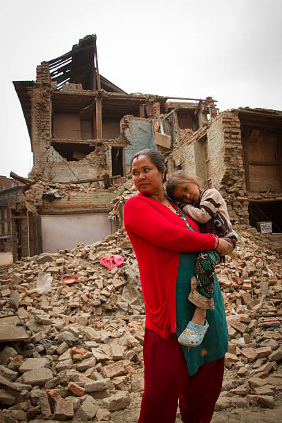 Mother and child outside earthquake ruined home, Bhaktapur, Nepal Bhaktapur, Nepal - May 9, 2015: Mother and child outside, earthquake ruined home, Bhaktapur, Nepal. Earthquake damage on the streets of Bhaktapur. Located 30km east of Kathmandu, the town was once rich with Buddhist and Hindu temples and a popular tourist spot for those visiting Kathmandu, Nepal thamel stock pictures, royalty-free photos & images