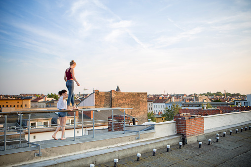 carefree summer day: young woman balancing on a railing on a roof, skyline in background