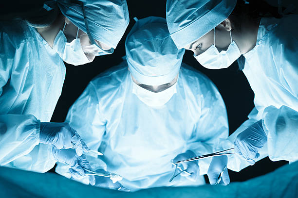 Medical team performing operation Medical team performing operation. Group of surgeon at work in operating theatre tonned in blue nurse smock stock pictures, royalty-free photos & images